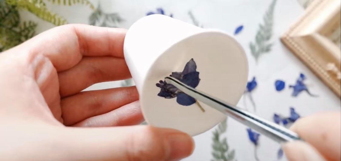 乾花蠟燭-1.第一步,首先把些少蠟溶掉,然後把乾花沾上一點點溶掉的蠟,為了牢固地把乾花黏在杯子上。然後,慢慢設計想要的花紋。最好用鉗子或夾子放進紙杯裏。