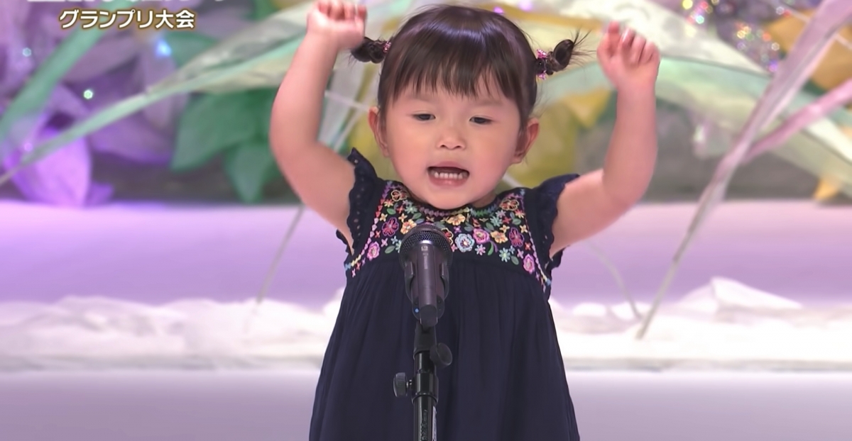 個子小小的乃乃佳身穿黑色連衣裙,綁著雙髮髻興致勃勃、毫不怯場地唱著歌曲。