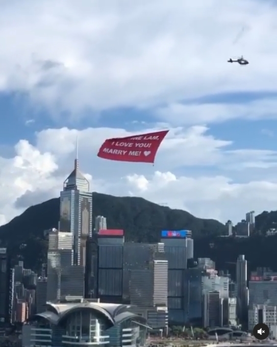 該張紅色橫額以白字寫上求婚字句「LOUANNE LAM，I LOVE YOU！MARRY ME！」於上空盤旋