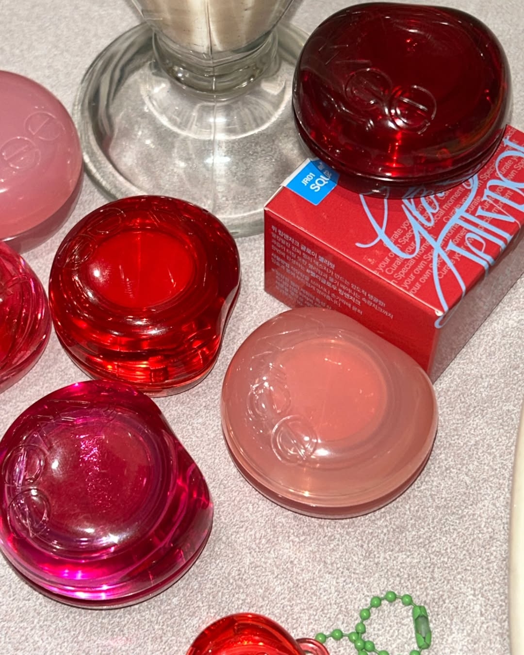 圖中展示的是fwee Lip & Cheek Glowy Jelly Pot 唇頰兩用光澤啫喱膏，其獨特的果凍質地輕按後能快速回彈，為雙唇和臉頰帶來統一的水潤光澤，大大提升妝容的和諧感。