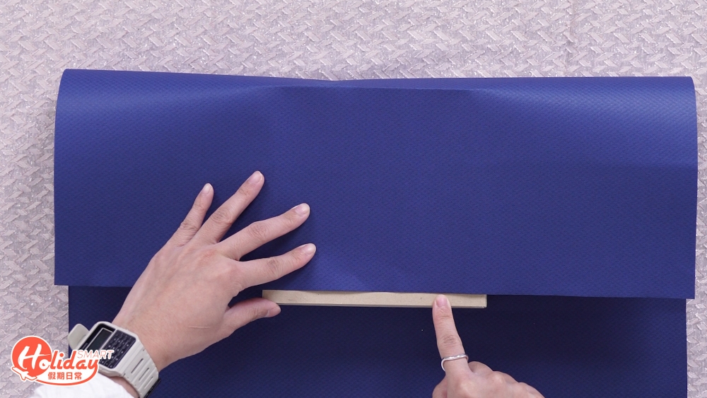 先將禮物橫放於花紙中央，從花紙上方貼着禮物盒摺至中間，預留約 1.5 cm 空間。