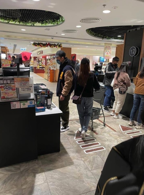 兩人似乎喺超市買完嘢，喺收銀處預備結帳。