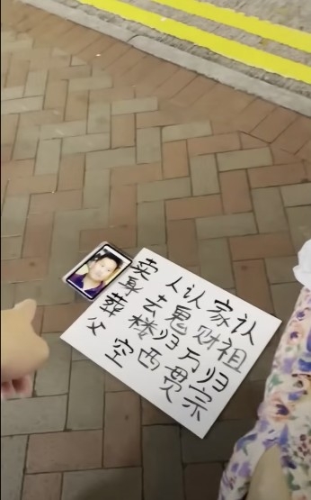 女子用簡體字寫「認祖歸宗,家財萬貫,認鬼歸西,人去樓空,賣身葬父」嘅紙牌