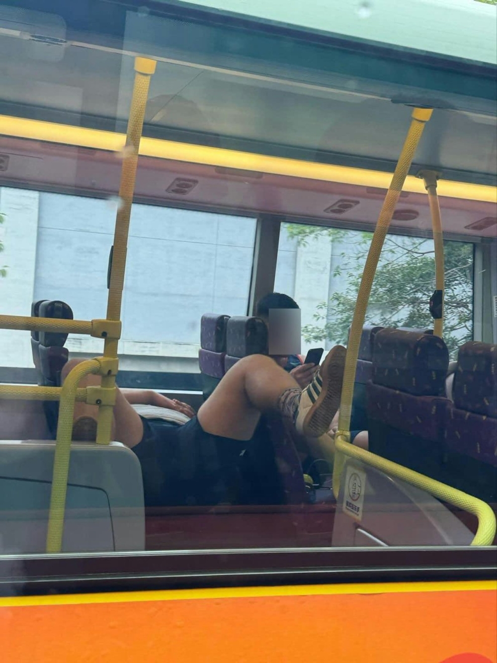 一名穿著短褲的男子橫躺於樓梯口的雙人座位，其雙腳張開分別踩於樓梯口左右兩邊扶手，姿勢十分張狂