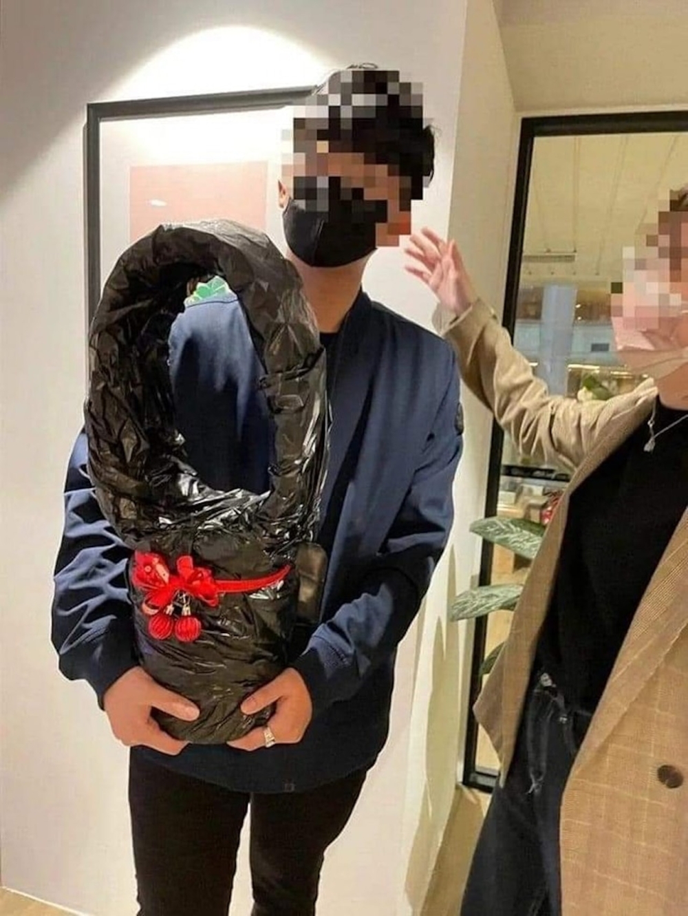 1名戴口罩穿深色外套男生,手捧着1份巨型禮物
