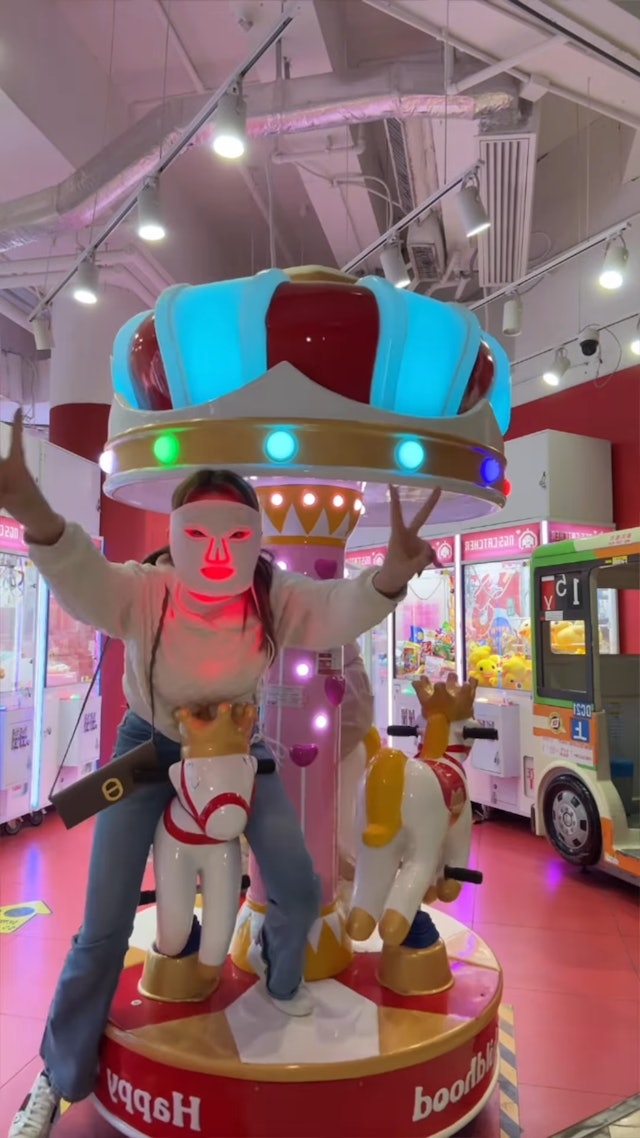 五索戴住LED光療面膜儀出鏡，並騎著遊樂場的旋轉木馬雙手比耶
