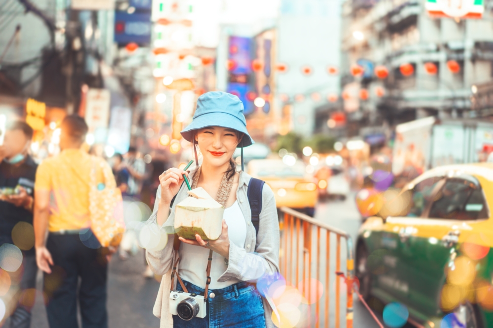 帶著笑容的女孩邊喝椰青邊逛夜市,燈光璀璨,人潮熱鬧,充滿異國風情!